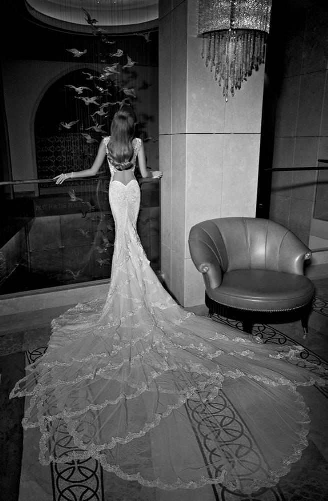 Galia Lahav's mermaid style Madison wedding dress has a colossal and dramatic train made from layers and ruffles of tulle and vintage lace. The back falls low with a heart shape. The sweetheart front is a marriage of two embroidered laces. The sides of the gown are layered with a sheer glittering fabric under an embroidered lace.