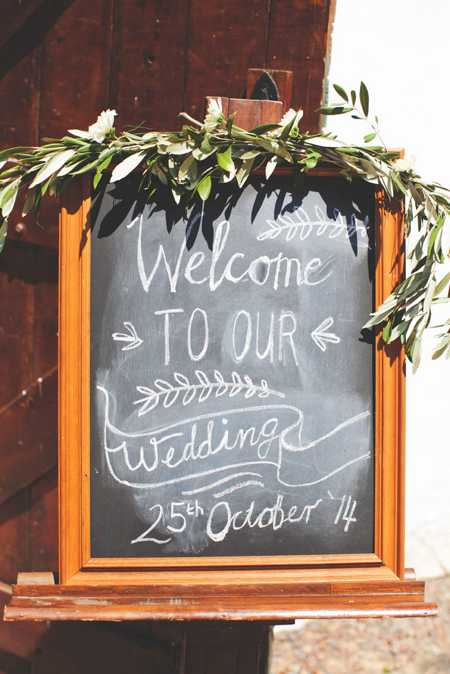 Welcome to our wedding chalkboard sign with laurel wreath. Groom in grey suit with grey tie. Green White Rustic South African Wedding // Justin Davis Photography
