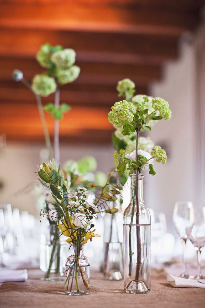 Single stem greens in mix and match bottles. Wedding reception decor. Green White Rustic South African Wedding // Justin Davis Photography