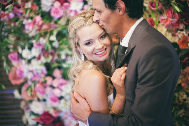 Stunning floral backdrop in pink and red. Groom in grey suit with grey tie. Green White Rustic South African Wedding // Justin Davis Photography