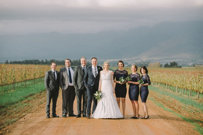 Bridesmaids in short navy dresses with long lace sleeves, groomsmen in navy suits with striped ties