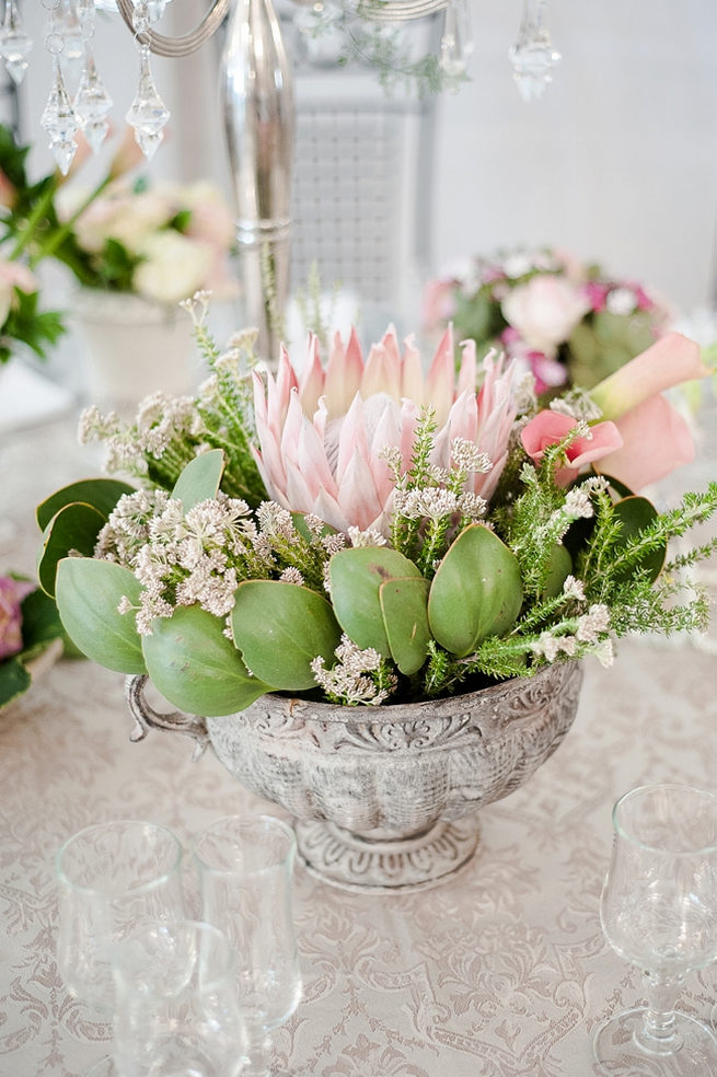 Wedding flower table arrangement: King Protea and greens in a vintage grey urn displayed on tables. Blush Pink and Powder Blue Spring Wedding // D’amor Photography