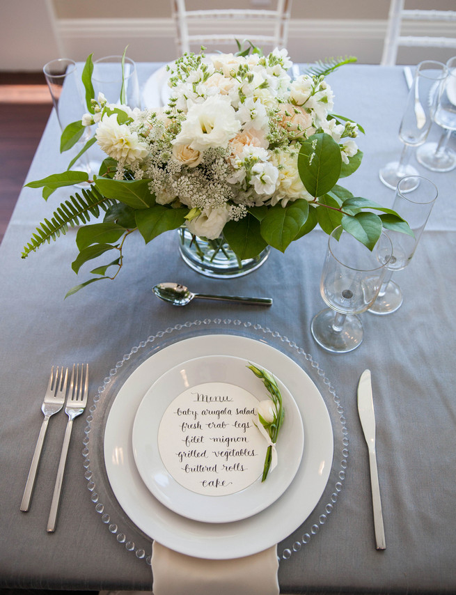 Hand calligraphed menu by Steele My Hear, place setting on clear glass charger and elegant fresh florals by Angel's Petals. Elegant Gray Blue Nautical Wedding by Rachel Capil Photography and Lindsay Lauren Events