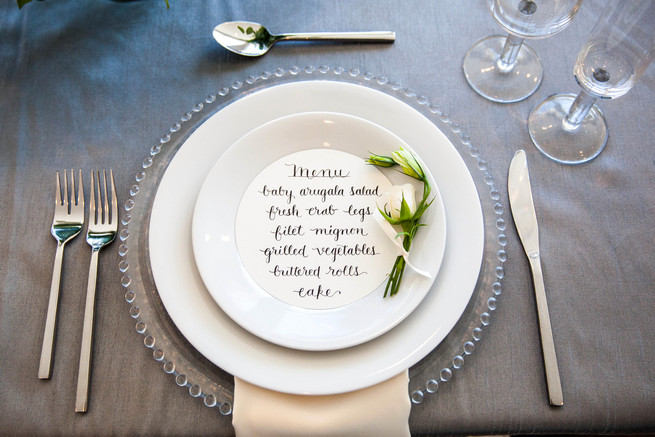 Hand calligraphed menu by Steele My Heart place setting on clear glass charger. Elegant Gray Blue Nautical Wedding by Rachel Capil Photography and Lindsay Lauren Events
