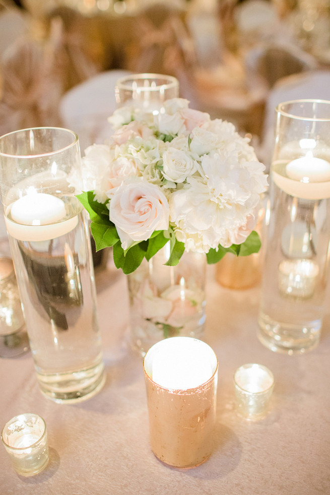 Chic Wedding reception florals of white hydrangea, blush roses, white roses and green fillers with white blossoms.  Clear glass vases with floating candles and silver votives.