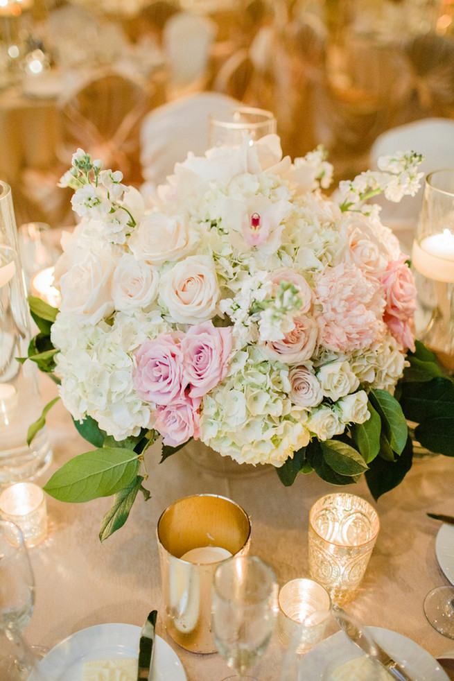 Chic Wedding reception florals of white hydrangea, blush roses, white roses and green fillers with white blossoms.  Clear glass vases with floating candles and silver votives.