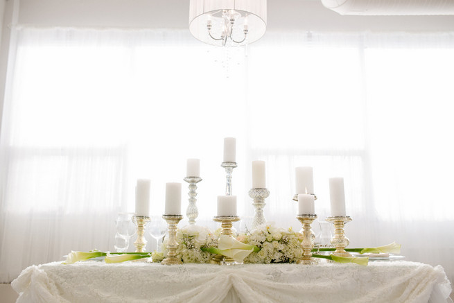 Gorgeous pillar candles. Super chic sweetheart table! White on White Glamorous Wedding Ideas by ENV Photography. Styled by Elegant Touches and Atmosphere Weddings