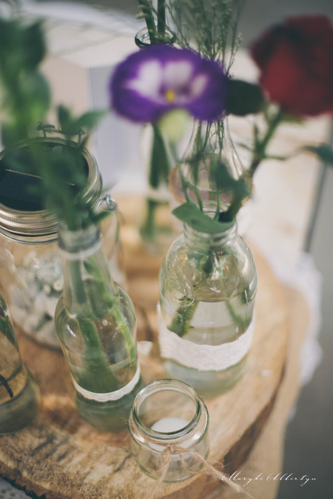 Rustic table decor with wood slabs, vintage bottles, lace and single stem roses.