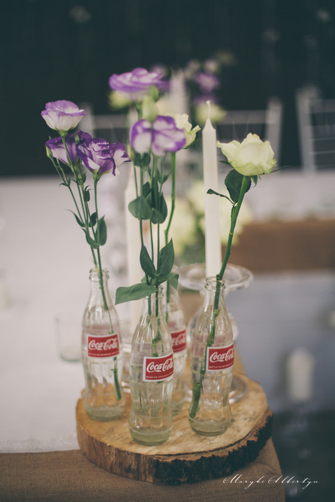 Rustic table decor with wood slabs, vintage bottles, lace and single stem roses.